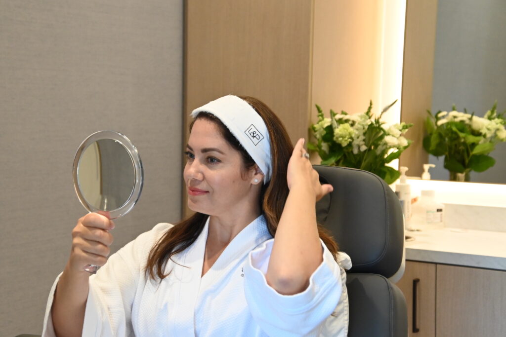 Woman holding mirror and looking at reflection while in a facial room